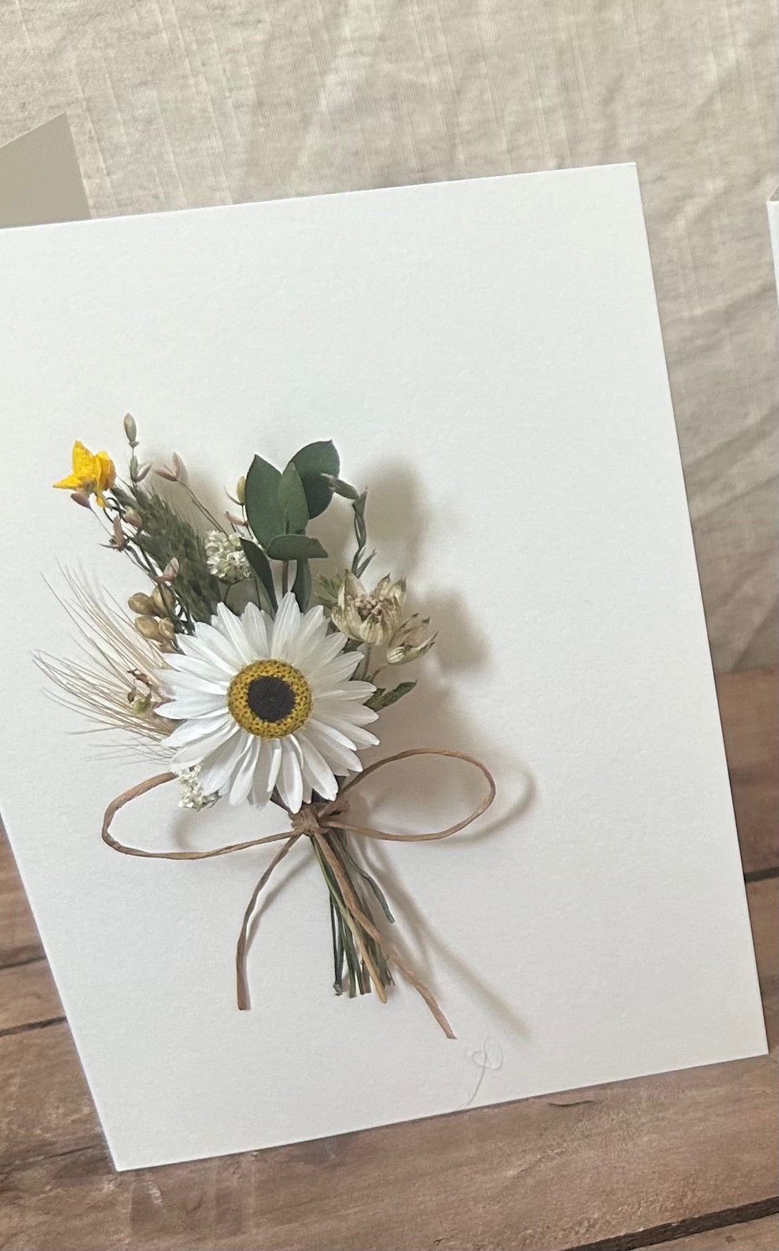 Floral corsage with a white flower and yellow center on a white card with a wooden surface background.